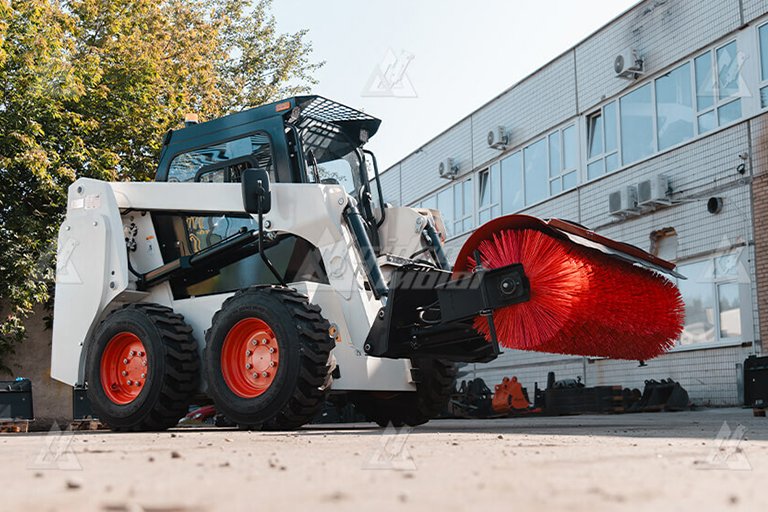 Bobcat skid steer with brush attachment sweeping construction site